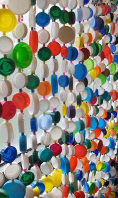 many colorful plates are hanging on the wall in this art work, which is made out of plastic cups and spoons