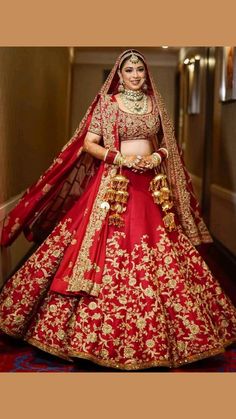 a woman in a red and gold bridal gown posing for the camera with her hands on her hips