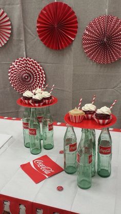 coca - cola bottles and cupcakes sit on a table with paper fan decorations