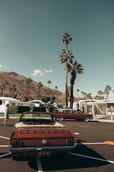 an old red convertible car parked in a parking lot with palm trees and rvs