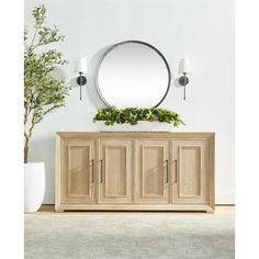 a large round mirror on the wall above a wooden sideboard with doors and drawers