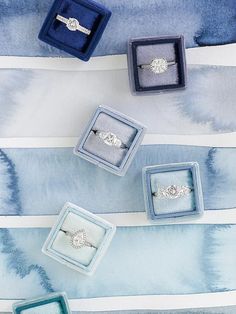 three engagement rings sitting in their boxes on a blue and white striped tablecloth with watercolor stripes