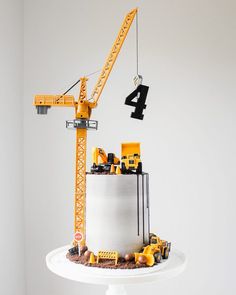 a birthday cake with construction trucks and cranes on top is displayed in front of a white wall