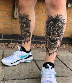 a man's legs with tattoos and sneakers on the ground next to a brick wall