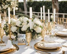 the table is set with white flowers and gold place settings