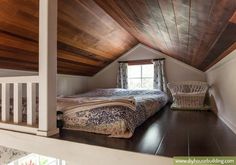 a bed sitting under a wooden ceiling next to a window in a room with white walls