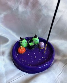 two little green monsters in a purple bowl with an antenna and some pumpkins on it