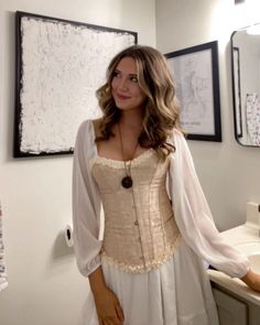 a woman standing in front of a bathroom mirror wearing a corset and dress