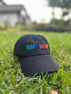 a black hat with the word plant daddy written on it in rainbow letters sitting in grass