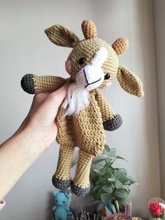 a hand holding a small stuffed animal in the shape of a giraffe on a table