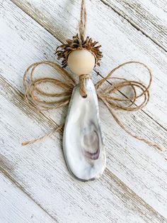 an angel ornament hanging from a string on a white wooden background with pinecone