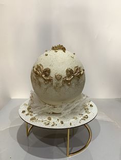 a white and gold vase sitting on top of a metal stand in front of a white wall