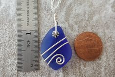 a penny is next to a blue sea glass pendant on a silver chain with a white swirl design