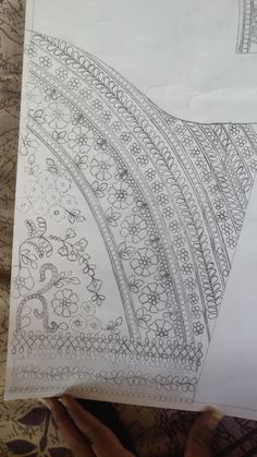 someone is holding up a piece of paper with intricate designs on it, and the bottom half has been drawn