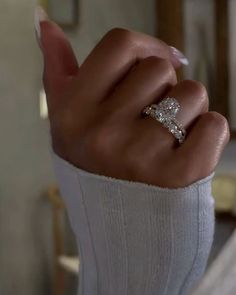 a woman's hand with a diamond ring on top of her finger, in a room