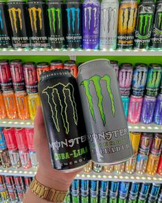 the monster energy drink is being held up by someone's hand in front of some colorful cans