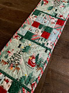 a quilted table runner with santa and reindeers on it, sitting on a wooden floor