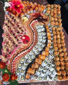 an assortment of sushi and other foods on a wooden platter with red flowers