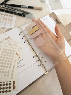 a person's hand on top of a binder next to some paper and markers