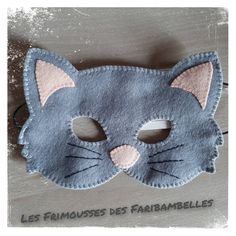 a gray cat mask with pink ears on top of a wooden table next to the words les frimosses des paribablelles