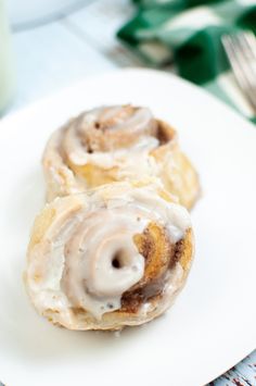 two cinnamon rolls on a white plate next to a glass of milk and silverware