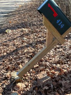 a wooden post with a mailbox on it in the middle of leaf covered ground