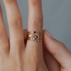 a woman's hand with a gold ring and four different colored stones on it