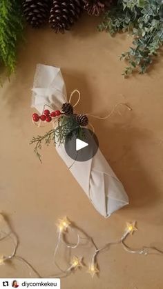 an ornament wrapped in white paper next to evergreen branches and pine cones