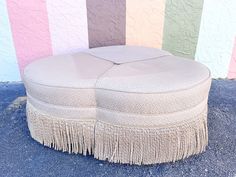 a round ottoman with tassels sitting on the ground in front of a multi - colored wall