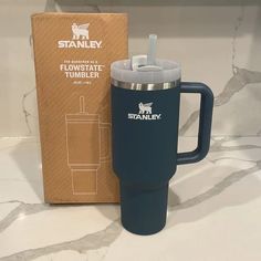 a blue travel mug next to a cardboard box on a marble countertop with the logo stanley