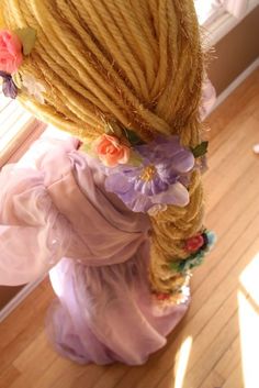 there is a very long hair doll with flowers on it's head, standing in front of a window