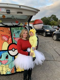 a woman holding a child in her arms while standing next to an open trunk with pokemon pictures on it