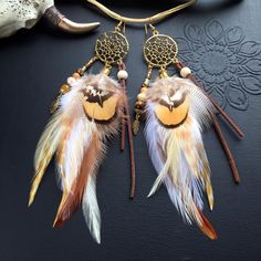 two brown and white feathers are hanging from gold ear wires on a black surface next to a cow skull