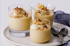 three desserts in small glass dishes on a white plate with spoons and utensils