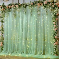 a green curtain with flowers on it and lights in the middle is decorated with pink roses