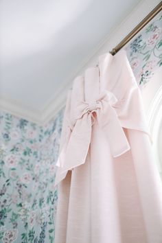 a pink curtain with a bow hanging from it's side in front of a floral wallpaper