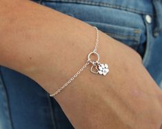 a woman wearing a silver bracelet with two clovers and a heart charm on it