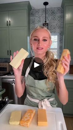 a woman in an apron holding two pieces of cheese on a cutting board and smiling