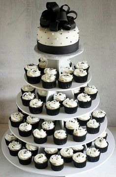 a three tiered wedding cake with cupcakes on the bottom and black bows on top