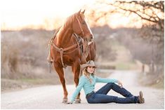 a woman sitting on the ground next to a horse