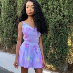 a woman standing in front of a bush wearing a purple and blue dress with flowers on it