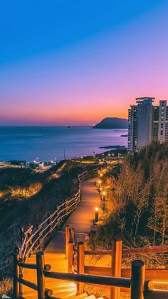 a wooden bench sitting on top of a beach next to the ocean at night with buildings in the background