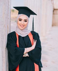 a woman in a graduation gown leaning against a column with her arms crossed and smiling at the camera