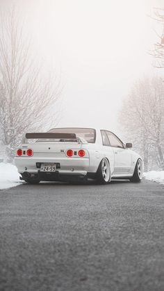 a white car parked on the side of a road covered in snow and ice with trees behind it