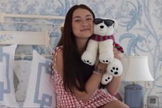 a woman holding a white teddy bear in her arms and smiling at the camera while sitting on a bed