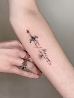 two hands holding each other with tattoos on their fingers and wrist, one has a flower tattoo on it