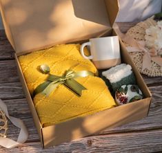 an open box with yellow towels and coffee mugs on the wooden table next to it