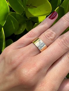 a woman's hand with a gold ring on top of it and green leaves in the background