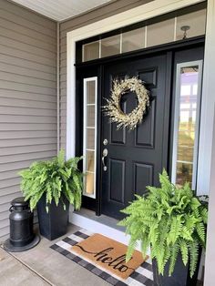 a black front door with two plants and a wreath on the porch next to it