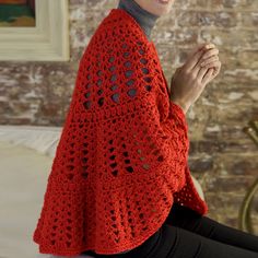 a woman wearing a red crocheted shawl sitting on a bed